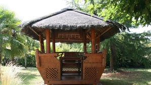 A wooden gazebo with a thatched roof, surrounded by lush greenery. - LUXURY VILLA ANGOULEME (Puymoyen)