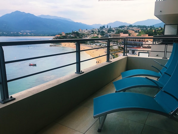 A balcony with blue chairs overlooking a beach and mountains.