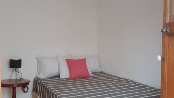 A bedroom with a bed, a bedside table, a lamp, and a wicker ceiling light.