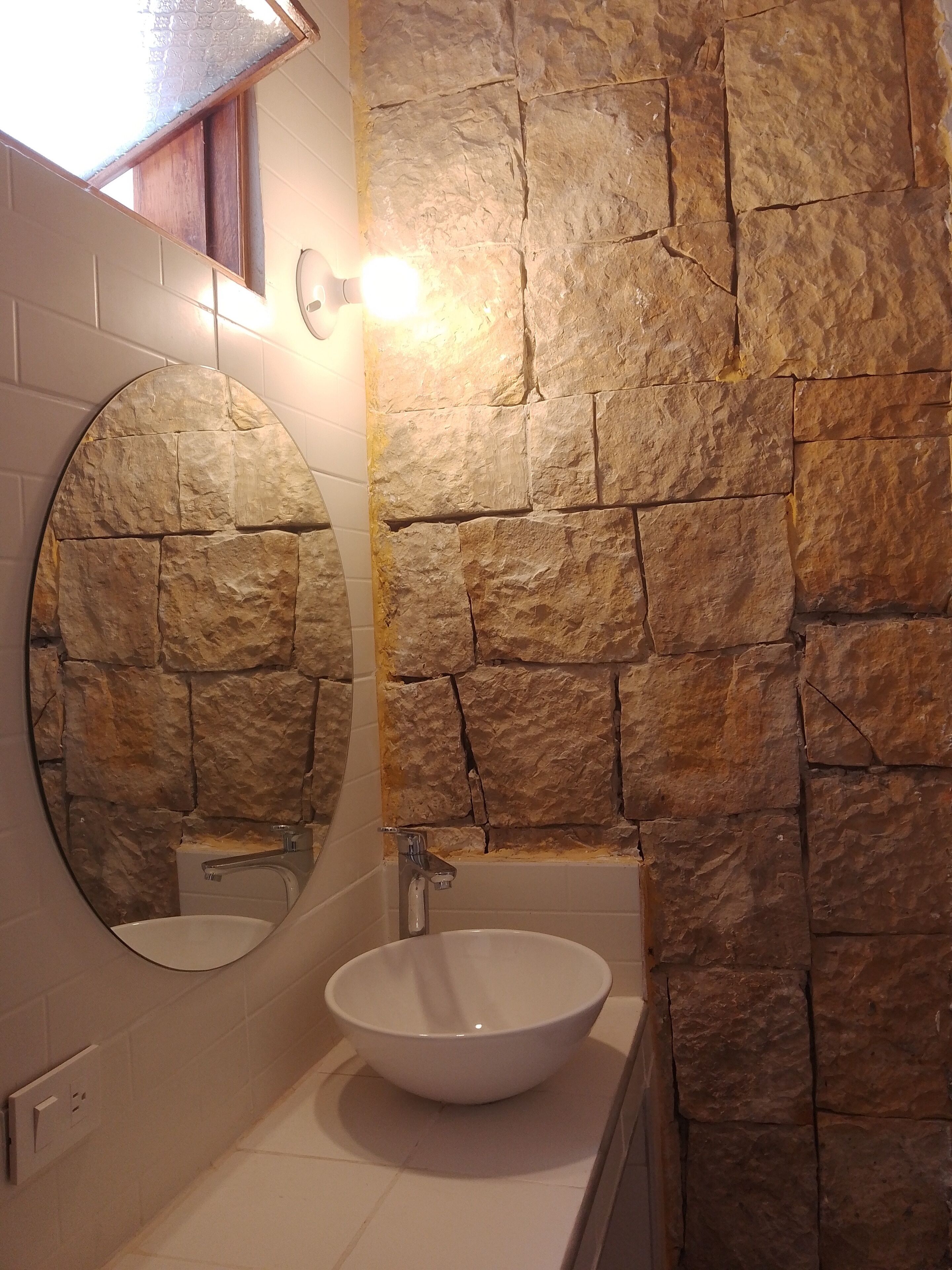 A bathroom with a stone wall, a round mirror, and a white sink.