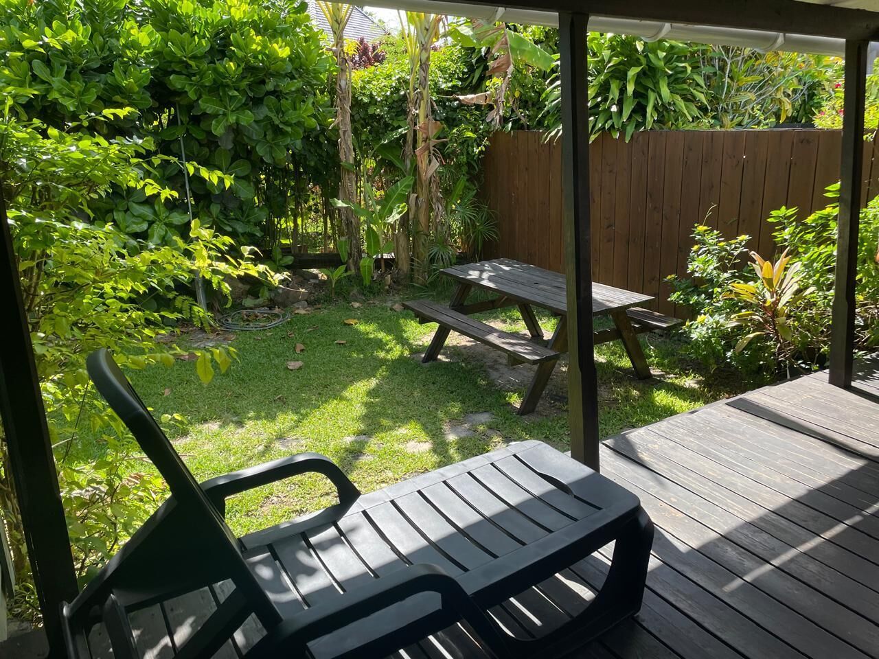 Une terrasse couverte avec une plateforme en bois, une table de pique-nique et une chaise en plastique verte.