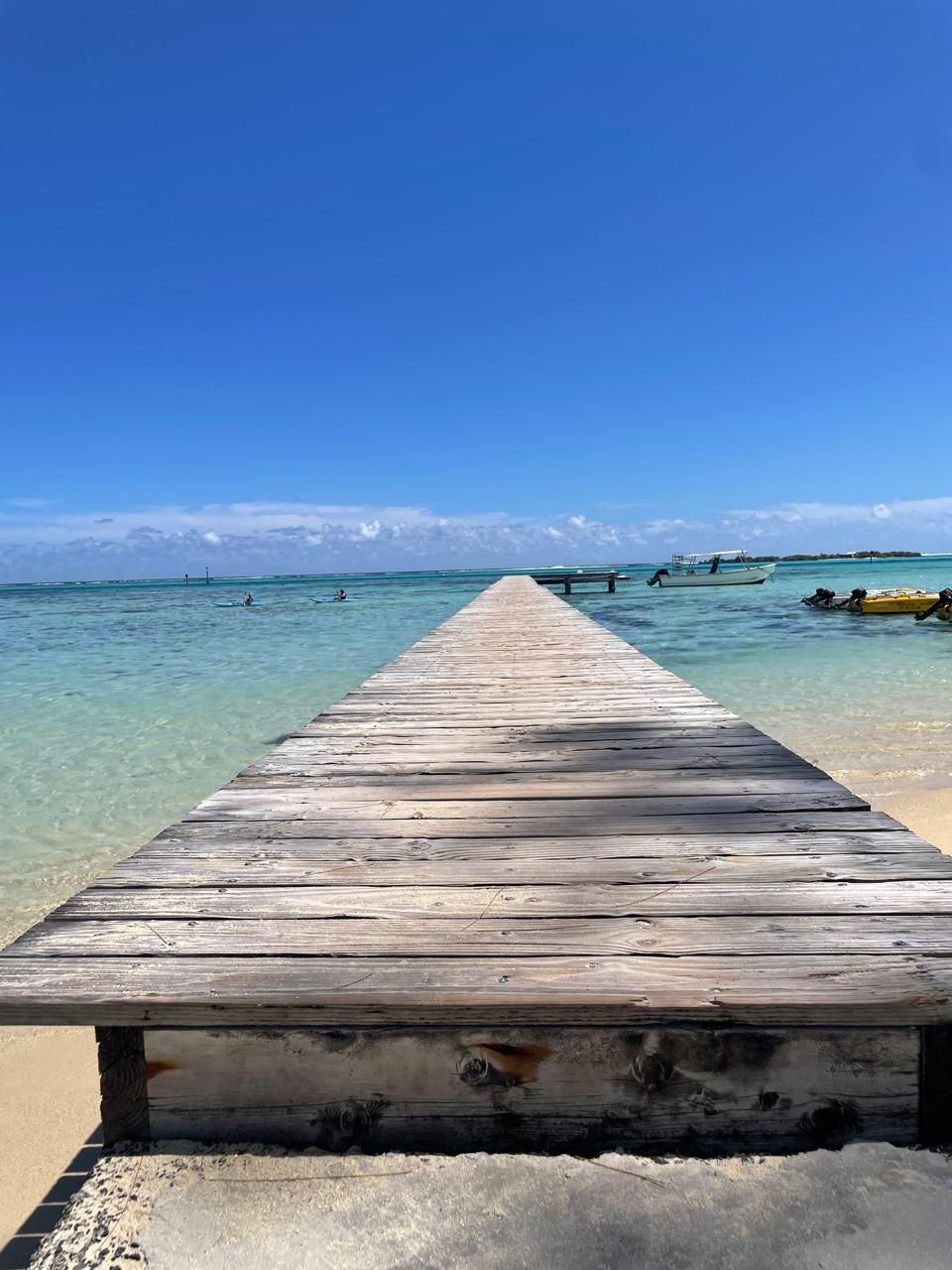 Un muelle de madera que se adentra en aguas turquesas cristalinas, con una playa de arena al final.