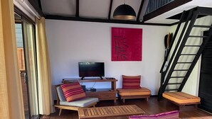 A modern living room with a flat-screen TV, wooden furniture, a red abstract painting, and a staircase.