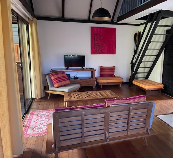A modern living room with a flat-screen TV, wooden furniture, a red abstract painting, and a staircase.