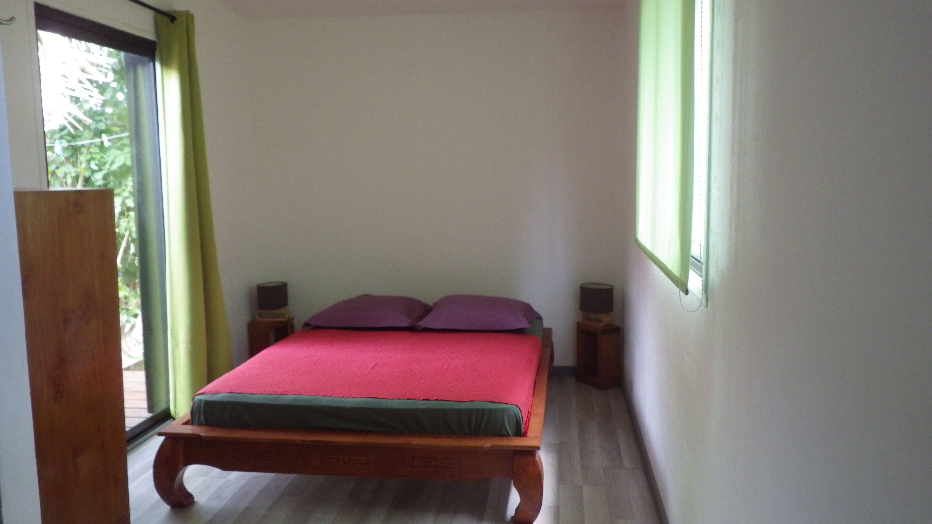 Une chambre à coucher avec un lit en bois, deux tables de chevet et une fenêtre avec des rideaux.