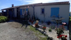 A two-story house with a tiled roof, a gravel driveway, and a garden with various plants and flowers. - House bungalow with garden and terrace, 1100m2 property, 8 person,  (Saint-Denis-D'oléron)