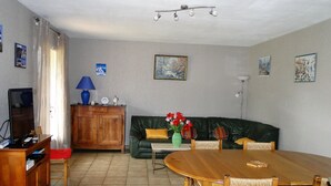 A living room with a wooden dining table, green leather sofa, and a TV stand. - House bungalow with garden and terrace, 1100m2 property, 8 person,  (Saint-Denis-D'oléron)