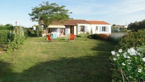 A two-story house with a tiled roof, a front porch with a table and chairs, and a well-maintained lawn. - House bungalow with garden and terrace, 1100m2 property, 8 person,  (Saint-Denis-D'oléron)