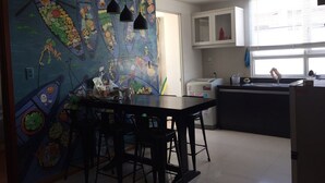 Une cuisine moderne agrémentée d’une fresque murale colorée, un coin repas avec des tabourets de bar et une fenêtre laissant entrer la lumière naturelle.