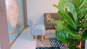 Un salon avec une carte accrochée au mur, un canapé, un fauteuil et une grande plante.