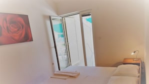Un dormitorio con una cama, una mesita de noche con lámpara y una puerta corredera que da a un balcón.