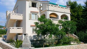 Un edificio de varios pisos con balcones, una antena parabólica y un muro de piedra.