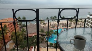 Un balcón con vista a la piscina de un resort, palmeras y una playa.