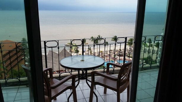 Un balcón con mesa y sillas, con vistas a una playa y una zona de piscina.