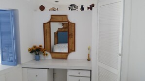 Una habitación blanca con un espejo de madera, un jarrón azul con flores y una puerta blanca cerrada.