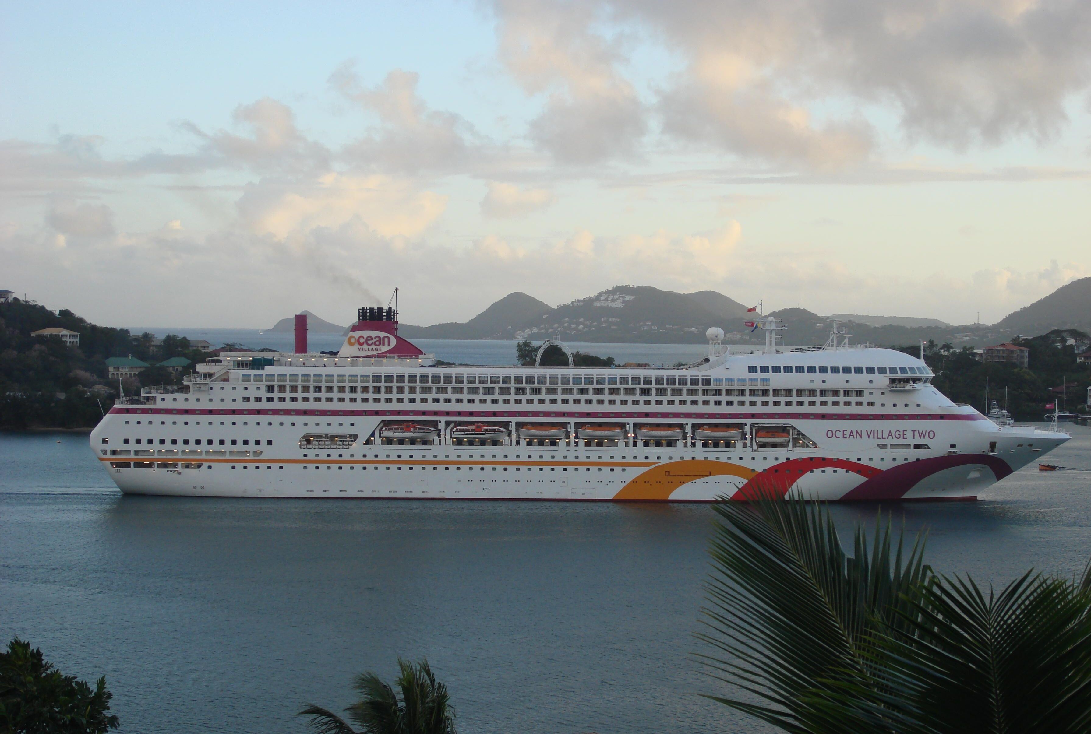 A large cruise ship named Ocean Village Two docked at a port with a backdrop of hills and a clear sky.