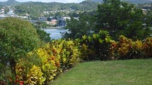 A view of a landscaped area with a river, buildings in the background, and a hilly landscape. - Affordable, Tranquil, St. Lucia Carnival, Bay View Apartment (Castries)