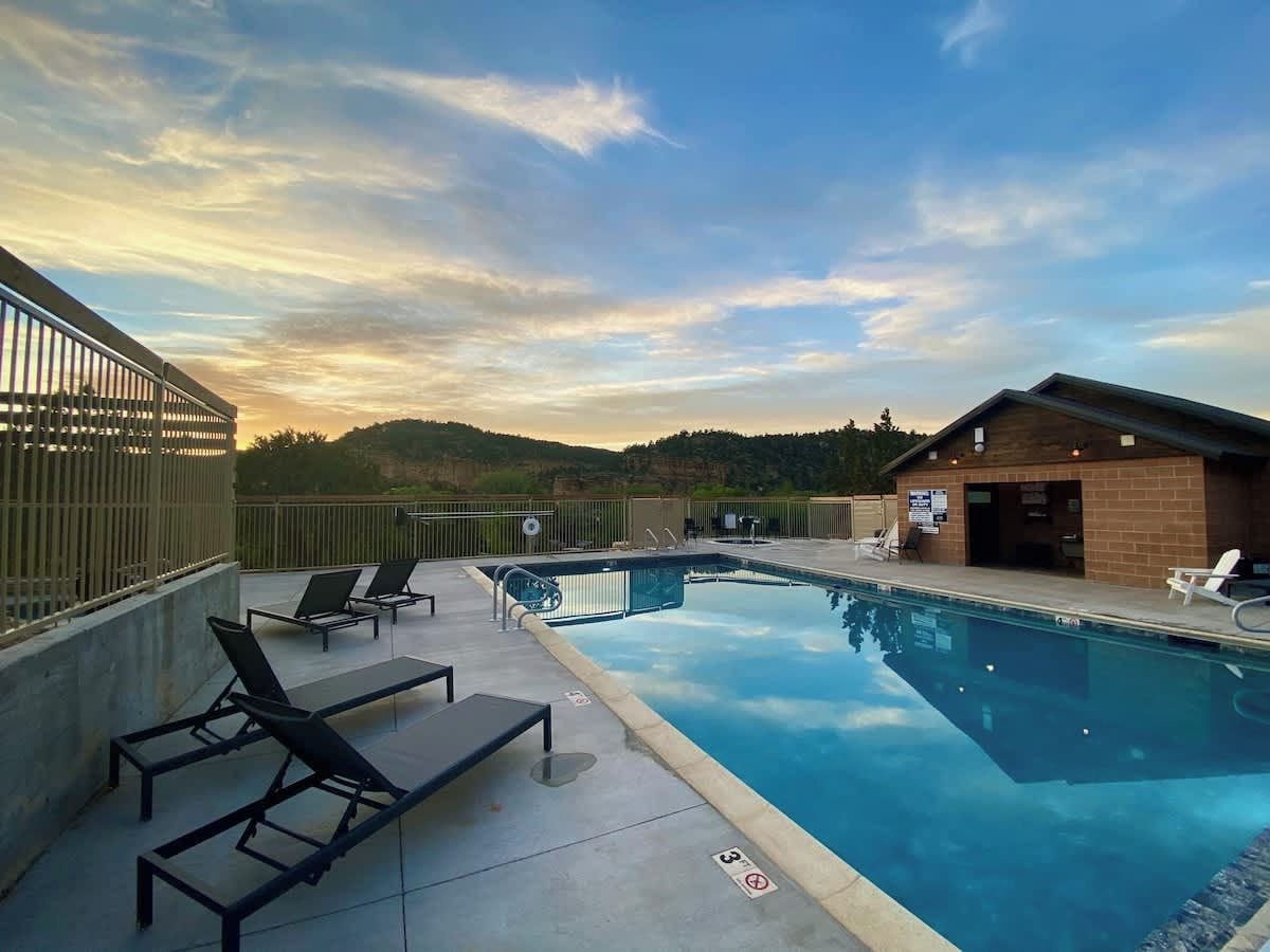 Une piscine avec des chaises longues, un bâtiment en briques et une vue sur les collines.