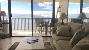 Un balcón con vista al mar, un sofá, una mesa y dos lámparas.