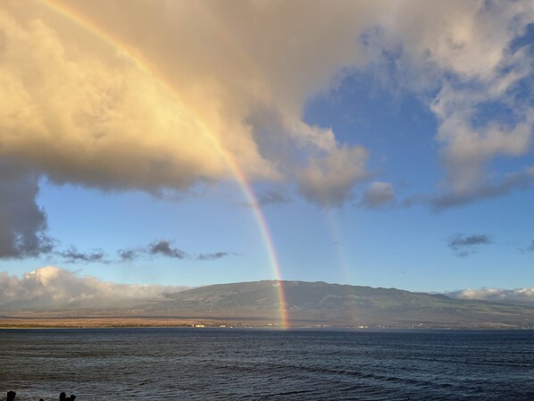 A coastal landscape with a rainbow over the sea and mountains in the background.