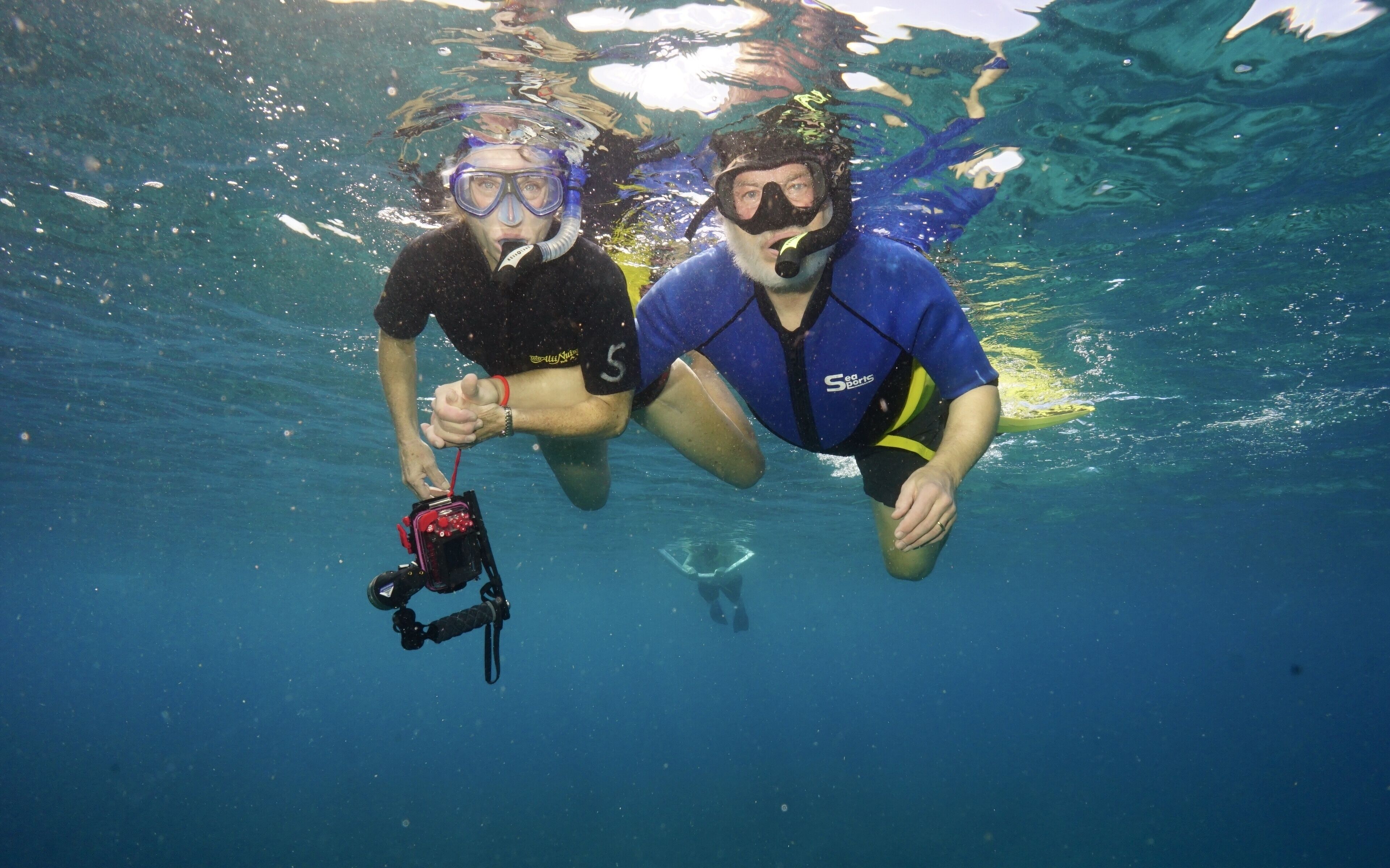 Dos personas haciendo snorkel bajo el agua, una sosteniendo una cámara.