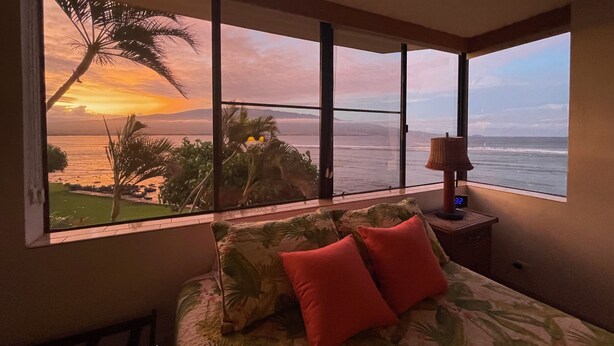 Un dormitorio con un ventanal grande que da a una playa y al océano al atardecer.