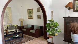 Een woonkamer met een bank, salontafel en decoratieve objecten. Er staat een plant in een pot, een lamp en een lijst met een afbeelding aan de muur.