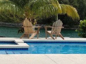 A poolside area with two wooden Adirondack chairs, a small table, and a potted plant with green leaves.