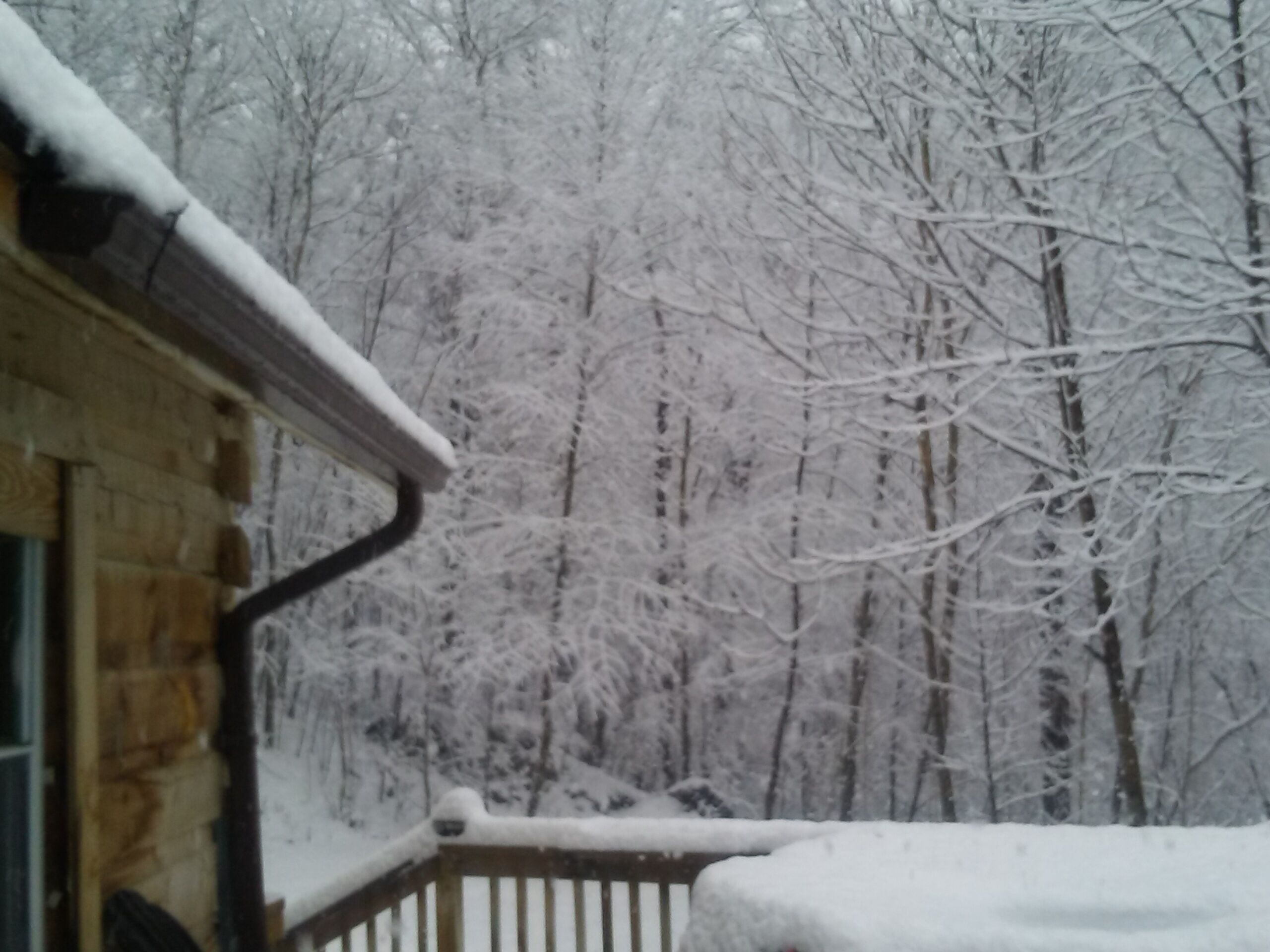 Une terrasse en bois dont les rampes sont recouvertes de neige, avec un bâtiment en pierre en arrière-plan.