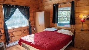 Ein Schlafzimmer in einer Holzhütte mit einem Bett, einem Kleiderschrank, einem Fenster mit Vorhängen und einem Nachttisch mit Lampe.