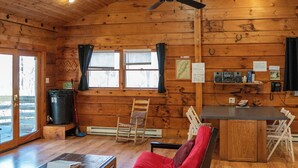 Ein Holzblockhaus-Interieur mit Essbereich, einer Couch, einem Deckenventilator und einer Küchenzeile mit Geräten.