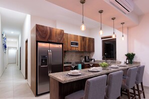 A modern kitchen with a stainless steel refrigerator, a built-in microwave, a granite countertop, and a bar seating area.