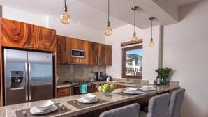 A modern kitchen with a stainless steel refrigerator, a microwave, and a stove. There are bar stools and a large island with a bowl of fruit. - Penthouse in the heart of Gringo Gulch (Puerto Vallarta)