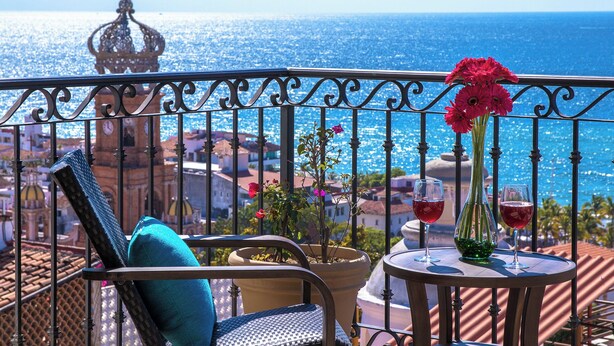 A balcony with a view of the sea, a chair, a table with two glasses, and a vase with flowers. - Penthouse in the heart of Gringo Gulch (Puerto Vallarta)