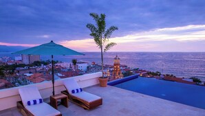 A rooftop terrace with a pool, lounge chairs, and a view of the ocean and cityscape at dusk. - Penthouse in the heart of Gringo Gulch (Puerto Vallarta)