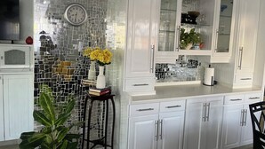 A kitchen with white cabinets, a tiled backsplash, a clock, and a potted plant. - The Palms Areca-Attractive, Alluring and Aesthetically artistic (Bridgetown)