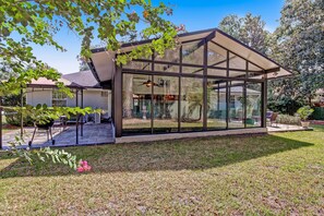 Une maison moderne dotée d’une grande baie vitrée, d’un patio avec mobilier d’extérieur et d’une pelouse bien entretenue.