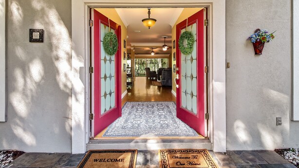 A house entrance with a red door, a welcome mat, and a doormat. - Luxurious Home w/ Spectacular Glass Room & Patios (Orange Park)