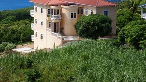 Un edificio de dos plantas con techo rojo, rodeado de vegetación y con vista a un cuerpo de agua.