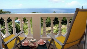 Un balcón con vista al mar, una silla amarilla y una mesa con tetera y tazas.