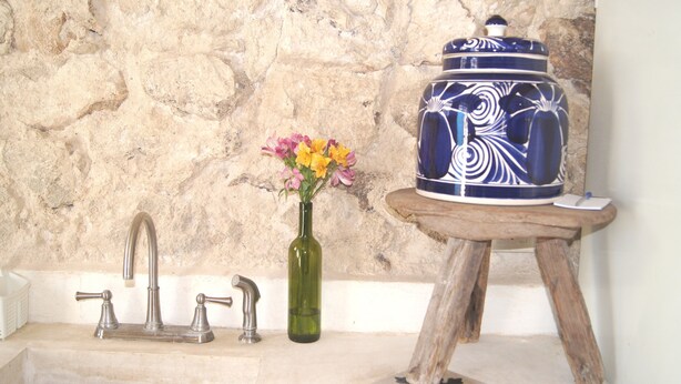 A bathroom with a stone wall, a green vase with flowers, a blue ceramic container, and a wooden stool.