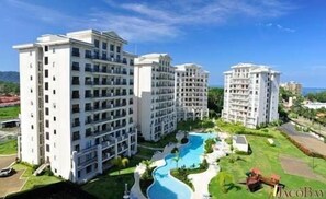 A high-rise hotel with multiple floors, a swimming pool, and a landscaped area. - Spacious 3 Bedroom Oceanview + Pool (Jaco)