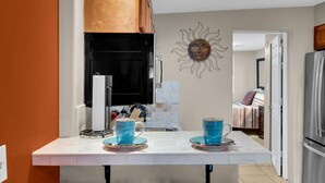 Una cucina con un piano di lavoro bianco, due tazze blu e un’opera d’arte a tema solare.