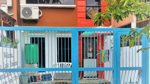 Un edificio residencial con fachada roja y naranja, una verja azul y una unidad de aire acondicionado visible.