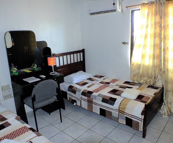 A small, tidy room with a single bed, a desk with a chair, a mirror, and a window with curtains.