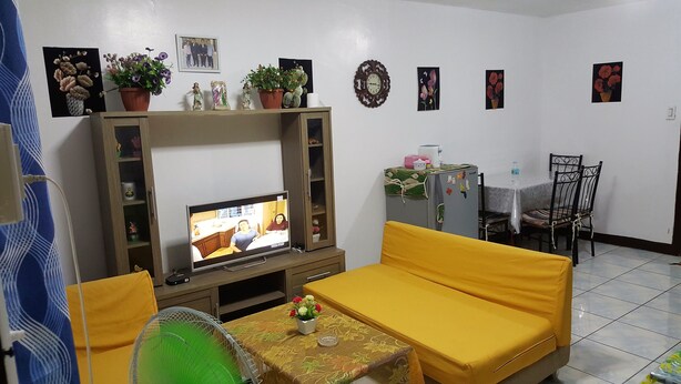 Una sala de estar con televisor, sofá amarillo y una mesa con un florero.
