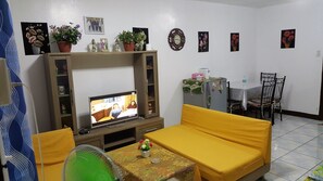 A living room with a television, yellow sofa, and a table with a flower vase.