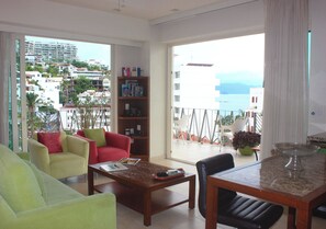 A spacious living room with a balcony, a dining area, and a bookshelf.