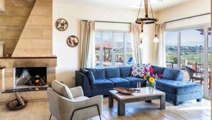 A modern living room with a fireplace, a blue sofa set, a coffee table, and a large window offering a city view.