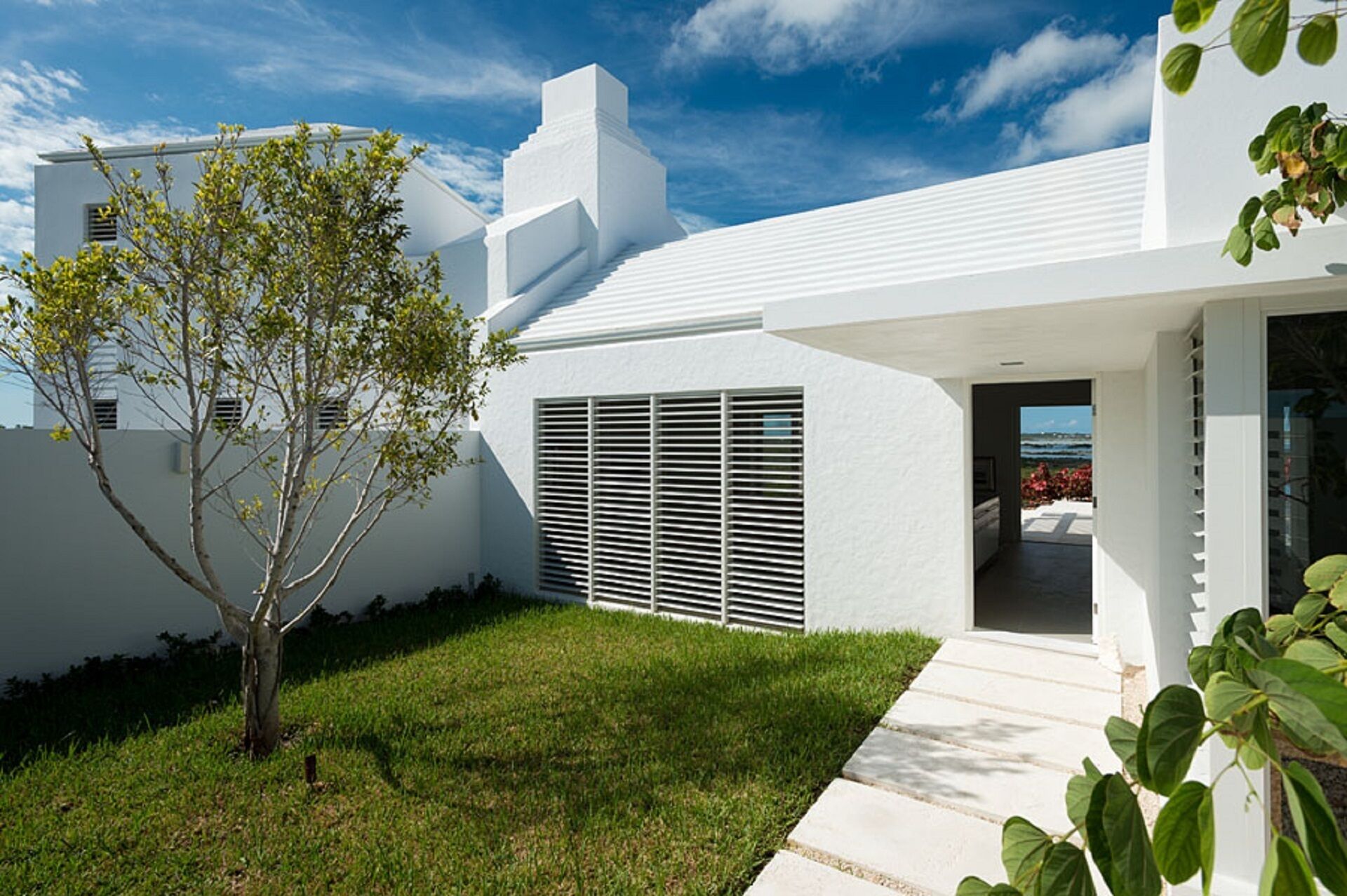 A modern white house with a clear view of the ocean through the doorway.